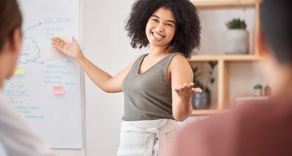 Business woman, whiteboard and presentation speaker in about us training, marketing workshop or office education in teamwork collaboration. Happy, creative mentor and coaching growth goals to workers.