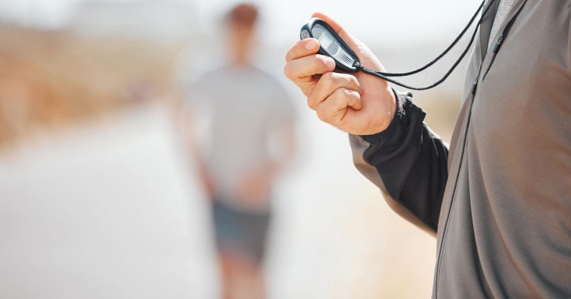 Fitness, coach and stopwatch of hands, time and runner speed and performance for record over blurred background. Hand of trainer in motivation for breaking times holding digital chronometer in sports.
