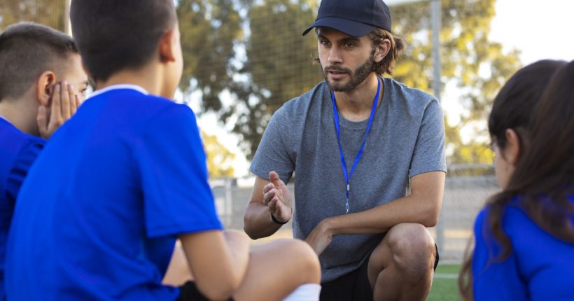 side-view-football-trainer-helping-kids