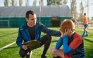 Coach comforting crying little soccer player after missed goal. Kids soccer football concept