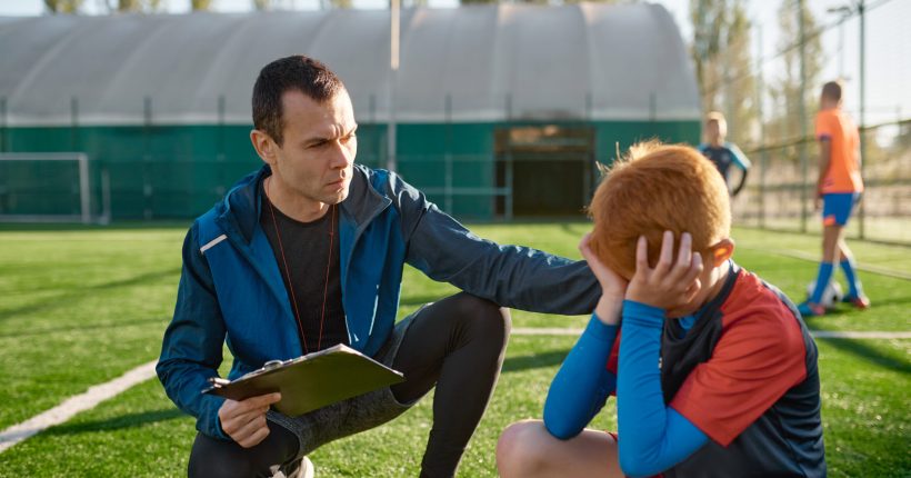 Coach comforting crying little soccer player after missed goal. Kids soccer football concept