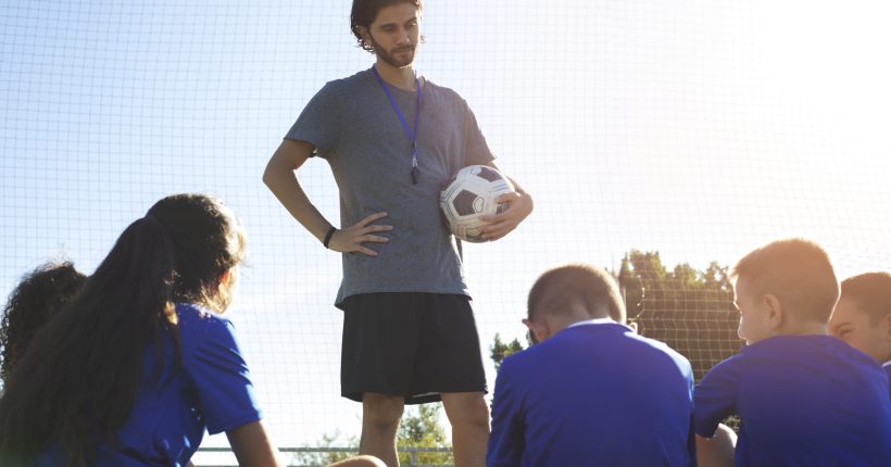 man-training-kids-playing-football-front-view