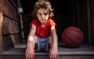 A young boy sitting on a wooden step with his hands in front of him